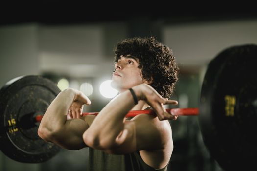 A young muscular man is doing hard training with barbell at the gym.