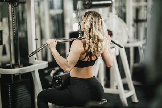 A young muscular woman is doing training on machine in the gym.