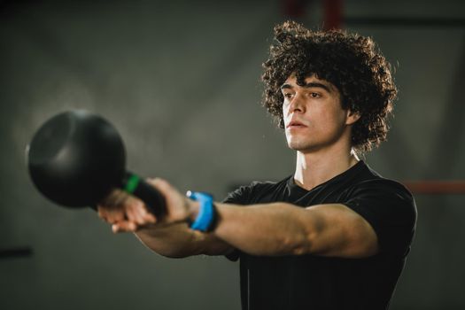 A young muscular man is doing hard training with kettlebell at the gym.