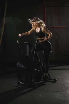 A young muscular woman is doing hard cal bike crossfit training in the gym.