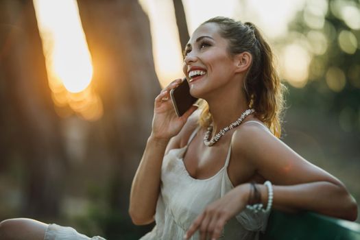 Young cheerful woman using a smartphone while enjoying on a bench in the park at summer vacation.