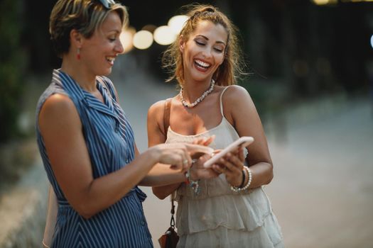 Two attractive young women are having fun and using a cellphone together while enjoying a summer vacation.