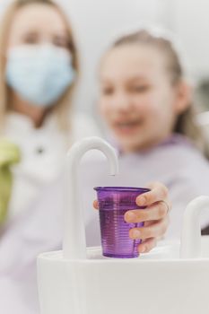 Close-up of a teenager girl  holding disposable water cup for mouthwash at the dentist. 