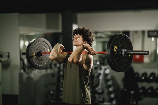 A young muscular man is doing hard training with barbell at the gym.