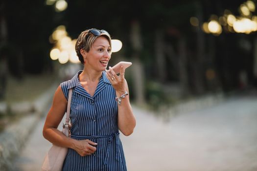 Mature attractive woman using a smartphone and enjoying a summer night walk.
