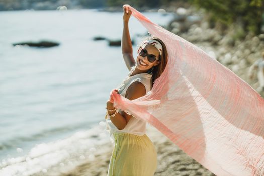 An attractive young woman holding scartf and having fun while enjoying a summer vacation on the beach.