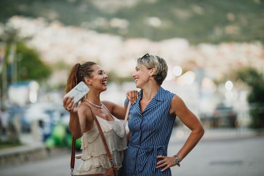 Two smiling women are having fun and enjoying in summer day while walking along the street of a Mediterranean town.