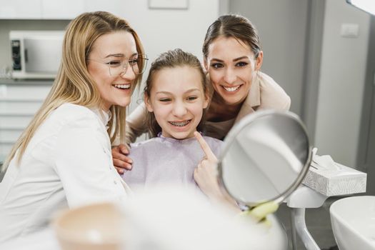 A happy teenager girl looking her teeth in a mirror after dental procedure at dentist's office.