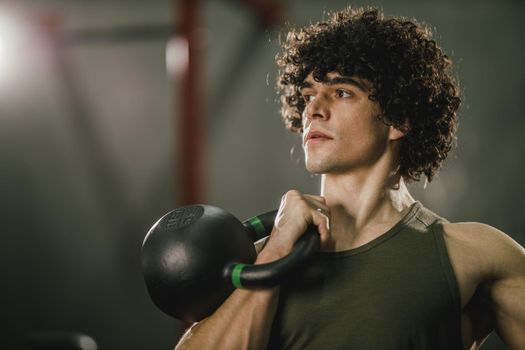 A muscular guy is doing hard training with kettlebell at the gym.