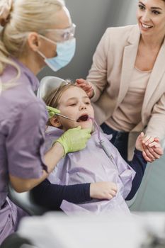 A cute little girl with her mom getting her teeth checked by dentist at dental clinic.