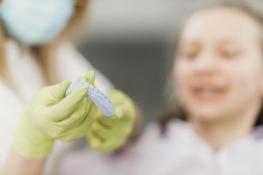 Close-up of an unrecognisable dentist holding dental plaster mould during consulting with teen girl patient in an office.