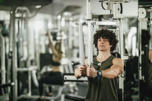 A young muscular man is doing training on machine in the gym.