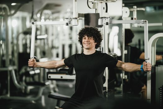 A young muscular man is doing training on machine in the gym.