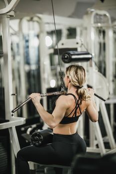 A young muscular woman is doing training on machine in the gym.