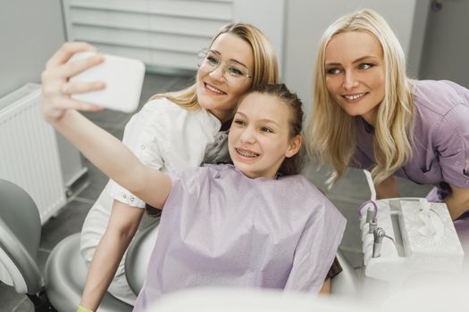 A happy teenager girl taking a sellfie with her dentist at dentist's office.