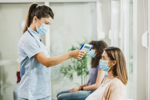 Young pregnant woman with a face mask having her temperature checked before coronavirus vaccine.