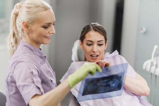 A young dentist and her female patient looking at orthopantomogram during dental appointment.