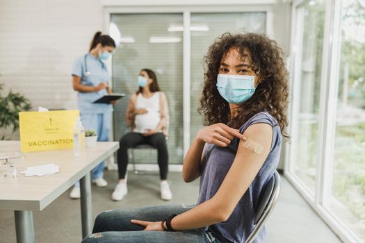 An African American teenager girl showing at her arm with a band aid after receiving the Covid-19 vaccine.