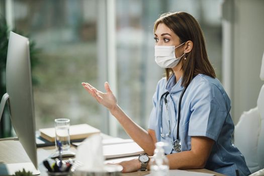 A young female nurse with protective face mask making a video call on a computer during COVID-19 pandemic.