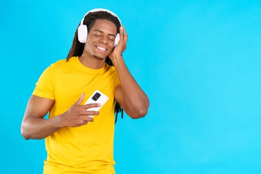 Latin man with dreadlocks listening to music with the eyes closed in studio with blue background