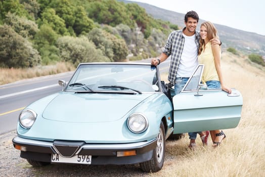 Theyre taking a trip together. A young couple standing alongside their convertible while on a road trip