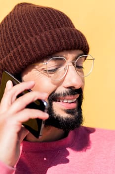 smiling young man talking on mobile phone in a yellow background, concept of technology of communication and modern lifestyle