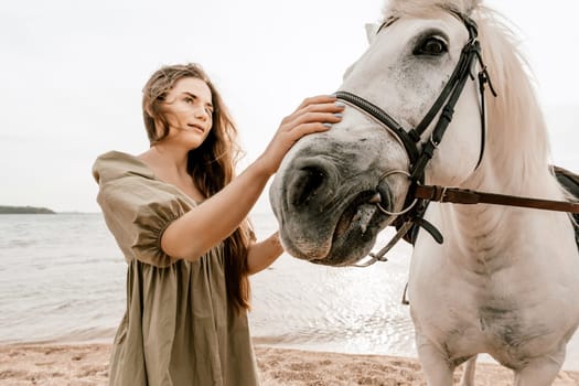 A woman in a dress stands next to a white horse on a beach, with the blue sky and sea in the background