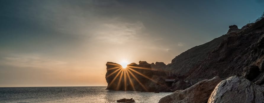 Banner. In blur An epic sunset on the sea - the sun sets behind the mountain and everything shines with warm light with long rays