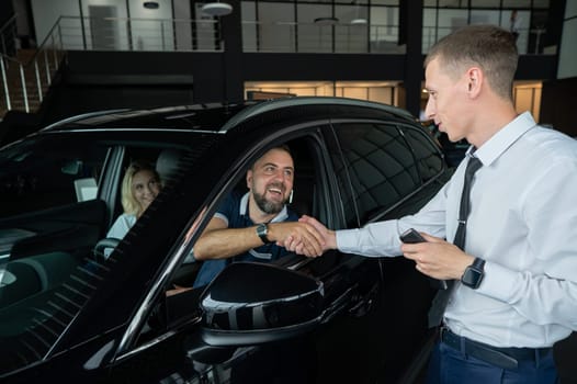 A caucasian couple shakes hands with a salesperson while buying a car