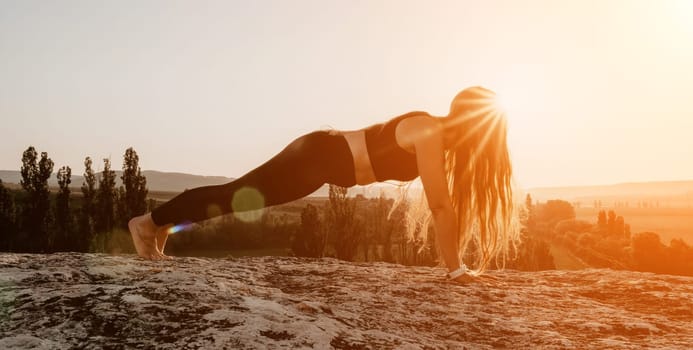 Well looking middle aged woman with long hair, fitness instructor in leggings and tops doing stretching and pilates on the rock near forest. Female fitness yoga routine concept. Healthy lifestyle.