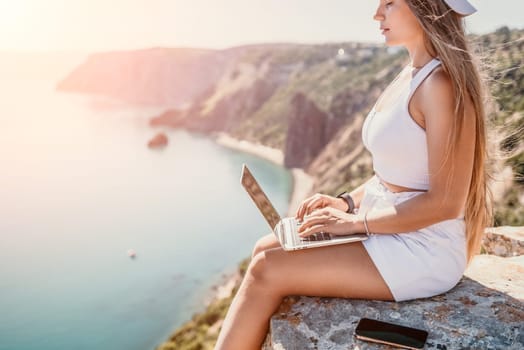 Digital nomad, Business woman working on laptop by the sea. Pretty lady typing on computer by the sea at sunset, makes a business transaction online from a distance. Freelance remote work on vacation