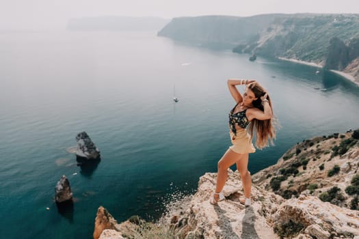 Woman travel sea. Happy tourist taking picture outdoors for memories. Woman traveler looks at the edge of the cliff on the sea bay of mountains, sharing travel adventure journey.