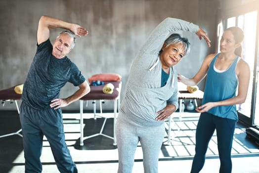 Stretching, help and old couple with personal trainer for fitness, wellness and physiotherapy. Health, workout or retirement with senior patient and physiotherapist in gym for warm up training.