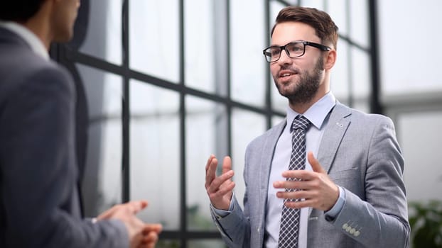 Two businessmen deep in discussion together while standing in an office boardroom with windows