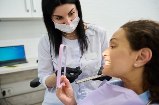 Female patient sitting in dentists chair, smiles looking at mirror while visiting dentist for teeth bleaching procedure. Teeth prosthesis. Teeth bleaching or whitening concept. Dental practice