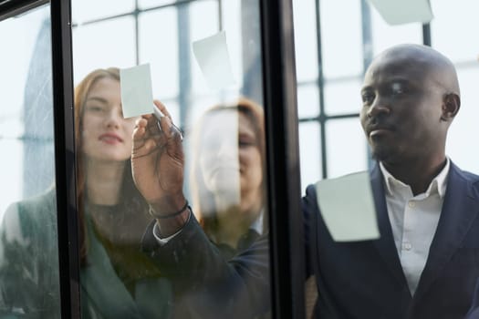 Creative business team looking at sticky notes on glass window