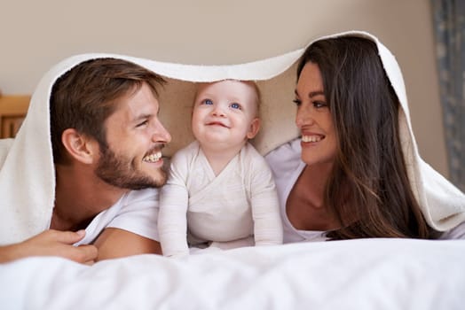Happy family, parents and baby with blanket on bed for love, care and quality time together. Mother, father and playful newborn child relaxing in bedroom with bedding fort, smile and bonding at home.