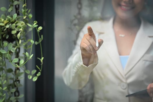 Smiling businesswoman holding pen and pointing on glass wall while standing at office. Human resource, hiring, employment concept.