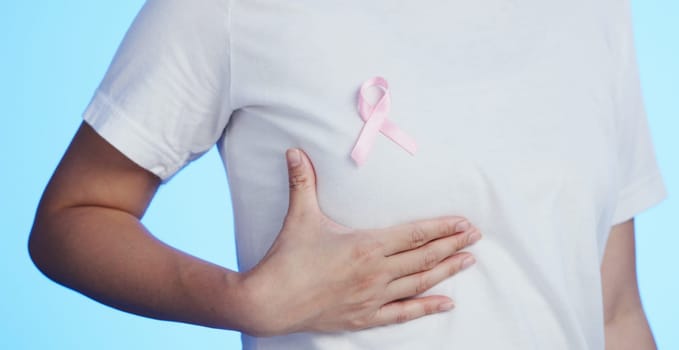 Pink ribbon, breast cancer and awareness with a woman in studio on a blue background for health. Chest, medical and healthcare with a female placing a bow, symbol or sign of recognition in october.