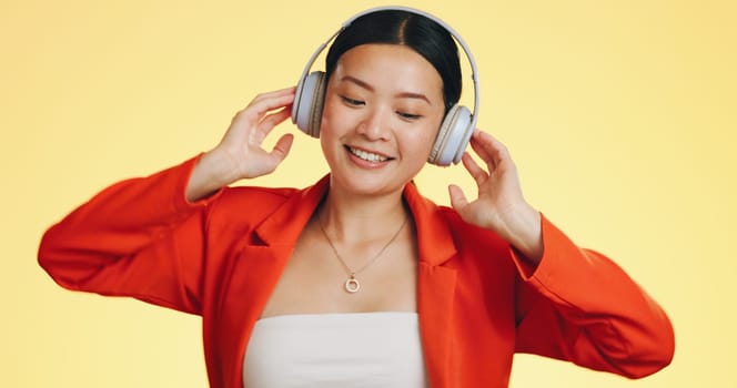 Dance smile, music headphones and Asian woman in studio isolated on a yellow background. Technology, podcast or happy female streaming, listening and dancing to radio, song and audio, sound and album.