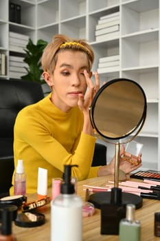 Charming young gay man blogger recording make up tutorial, live streaming at home. LGBTQ lifestyle, influencer, blogger.