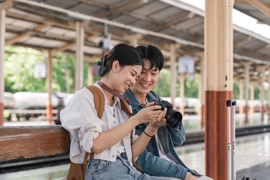 Beautiful couple at railway station waiting for the train. A young woman and a man are sitting and looking at pictures taken by cameras at a train station.