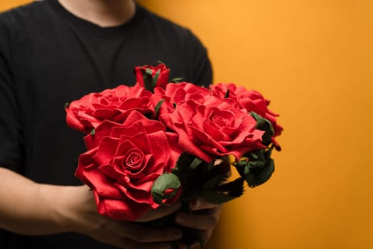 Cropped image of man hands holding bouquet of red roses over yellow background with space for text.