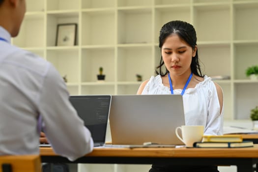 Focused female employee working on laptop, preparing presentation at office desk.
