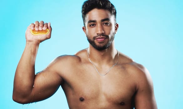 Skincare, squeeze and face of man with orange in studio for beauty, wellness and citrus treatment on blue background. Fruit, facial and portrait of indian guy model with organic, anti aging vitamin c.