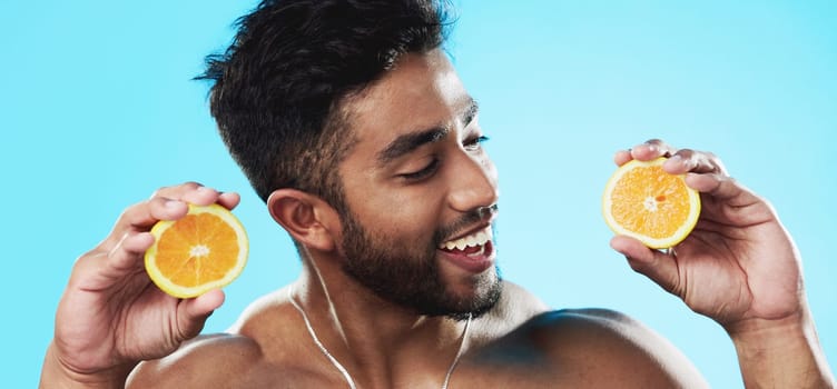Orange, skincare and face of man in studio for beauty, wellness and citrus treatment on blue background. Fruit, facial and portrait of indian male model excited for organic vitamin c skin cosmetics.