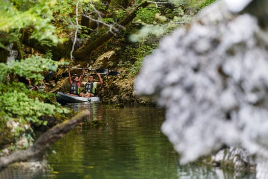 A young couple enjoying an idyllic kayak ride in the middle of a beautiful river surrounded by forest greenery.