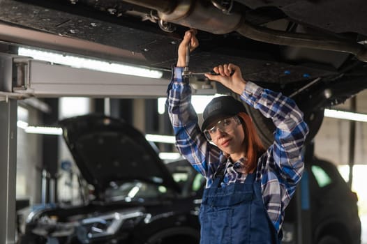 Female mechanic unscrew the nuts on the bottom of the car that is on the lift. A girl at a man's work