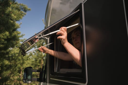 The girl opens the window of the van to enjoy the sun. The concept of people traveling on summer holidays inside a car-camping, mobile home.