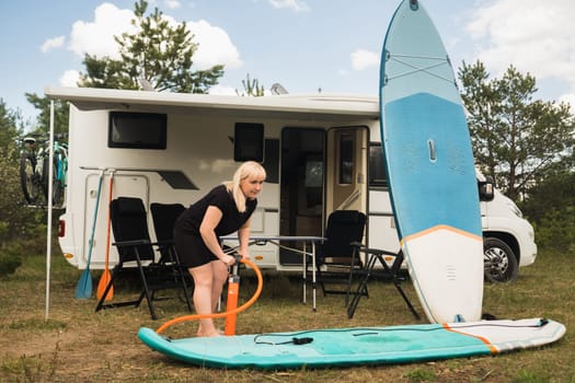 A woman inflates a sup-board for swimming near her motorhome.